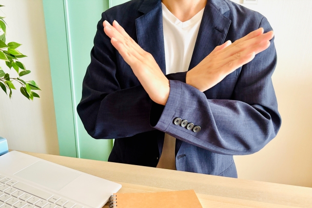 手で×をつくる男性